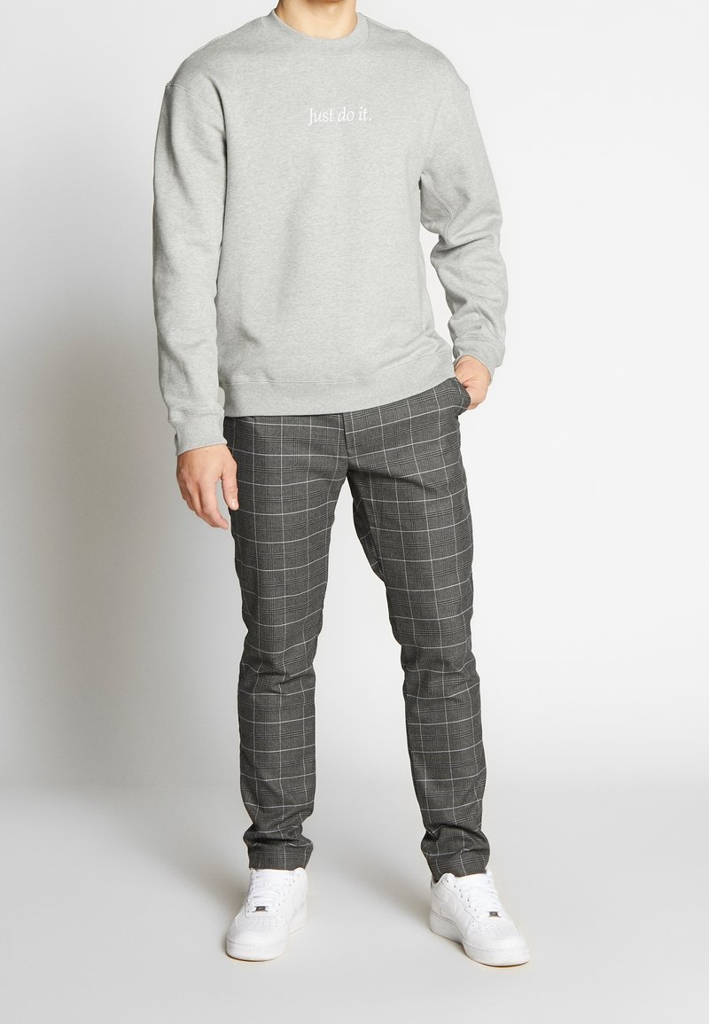 Šedá mikina s bílým nápisem "Just do it.", kombinovaná se štíhlými šedými kostkovanými kalhotami a bílými teniskami, s hladkou texturou.