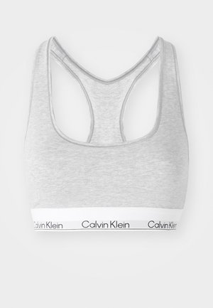 Grå sportsbh med racerback-design, laget av mykt materiale, med et hvitt elastisk bånd med "Calvin Klein"-tekst nederst.