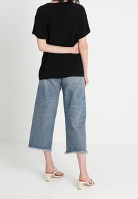 Zwarte, loszittende t-shirt gecombineerd met lichtblauwe, wijde denim jeans met uitgescheurde zomen en witte blokhak sandalen.