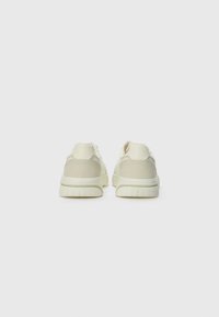 White sneakers with a smooth texture, featuring a mix of materials and a streamlined shape. The heel has a subtle gray accent.