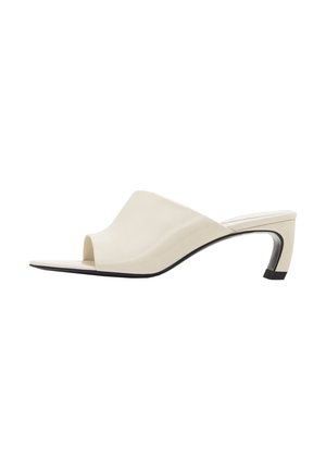 Mules ouvertes beige en cuir lisse. Présentent un design ondulé sur le dessus, un petit talon courbé et un accent de semelle noire.