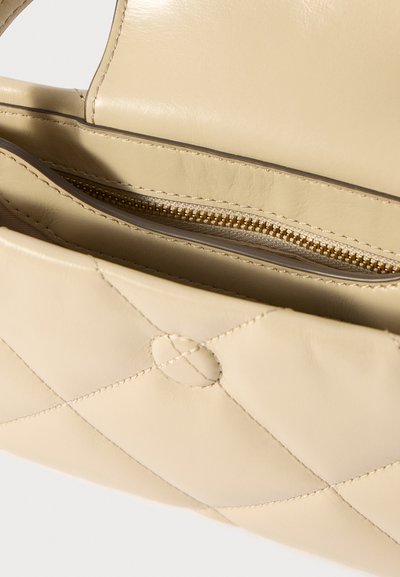 Ανοιχτή μπεζ δερμάτινη κουβερντούρα τσάντα που δείχνει την εσωτερική τσέπη με φερμουάρ χρυσού χρώματος και λεπτομερή ραφή.