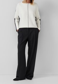 Pull blanc avec des panneaux latéraux noirs, présentant un col rond et une couture verticale. Associé à un pantalon large noir, coupe ajustée.