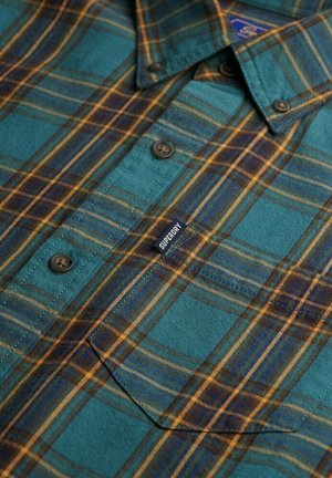 Camisa de cuadros en tonos verde azulado y marrón, con botones, un cuello y una etiqueta de logotipo visible. El material parece suave con un acabado texturizado.