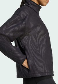 Veste à col haut noire en pull, avec un motif zébré texturé, des manches longues et des poches latérales. Fabriquée en tissu doux.