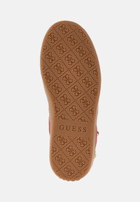 Semelle de chaussure en caoutchouc présentant une couleur beige avec un motif en losange embossé portant le logo "G" et le mot "GUESS" centré.