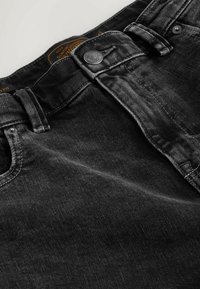 Black denim jeans feature a button closure, belt loops, and a faded texture. The fabric is sturdy with visible stitching and a brand tag.