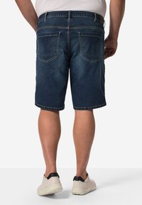 Shorts en denim bleu foncé avec une coupe droite ; dotés de deux poches arrière avec des coutures contrastées et des bords ourlés. Associés à des sneakers claires.