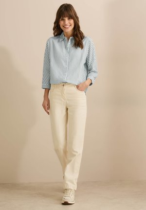 Chemise à boutons rayée bleu clair avec une coupe décontractée, associée à un pantalon droit crème et des baskets beiges. Fond neutre.