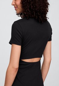 Črno kratka majica z rokavi. Ima izrez na hrbtni strani. Iz mehke, raztegljive bombažne tkanine. Gladka tekstura.