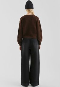 Bruine gebreide trui met kabelgebreide mouwen, gecombineerd met een hoge taille zwarte brede broek; van achteren bekeken.