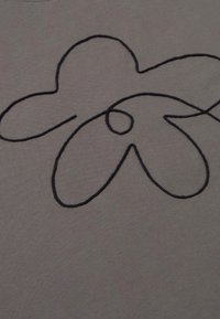 Grauer Stoff mit einem schwarzen, bestickten Blumenmuster, das ein rundes Zentrum und verlängerte Blütenblätter zeigt, mit einer glatten Textur und einfachen Linien.