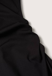 Tissu noir avec des plis doux posé sur un fond gris clair, montrant la texture et les détails du drapé.