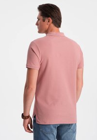 Pikétröja i mjuk rosa tyg, korta ärmar och en klassisk krage. Har sidsprund och ryggslits för extra komfort. Bärs med blå jeans.