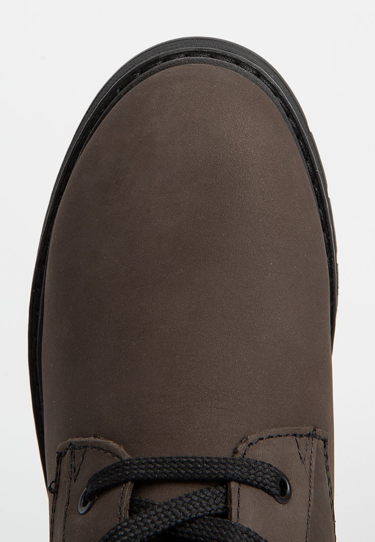 Zapato de cuero marrón con punta redondeada, cordones negros y un acabado texturizado. Presenta una suela de goma y costuras en contraste.