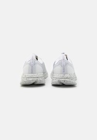 Chaussures de sport blanches avec une tige en mesh texturé, une semelle en caoutchouc tachetée et un soufflet de traction. Présentent un marquage subtil au talon et à la languette.