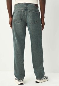 Jean large bleu foncé avec une texture douce, dotés de deux poches arrière, de détails cousus et d'une étiquette en cuir à la taille.
