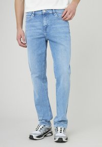 Jeans en denim bleu clair à coupe slim, présentant un design classique à cinq poches, des passants de ceinture et une fermeture à bouton. Portés avec des baskets grises.