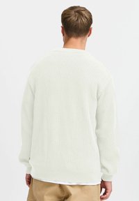 Hvit ribbestrikket genser med en avslappet passform, med rund hals og lange ermer. Teksturen er myk, med en litt løs vev.