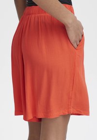 Heldere oranje shorts van een zachte, gestructureerde stof. Voorzien van een elastische tailleband en zijzakken. De zoom is licht gebogen.