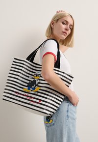 Sac fourre-tout à rayures noires et blanches mettant en avant un personnage de dessin animé, avec un graphique coloré et un texte rouge en bas. Matériau en tissu, taille moyenne.