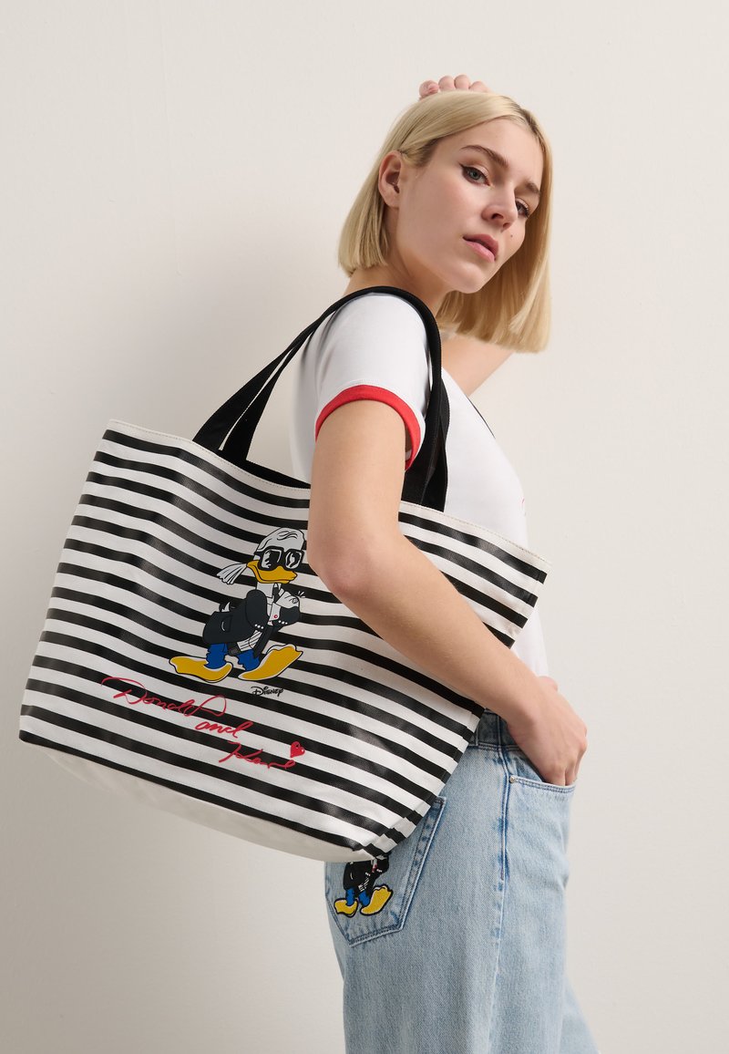 Sac fourre-tout à rayures noires et blanches mettant en avant un personnage de dessin animé, avec un graphique coloré et un texte rouge en bas. Matériau en tissu, taille moyenne.