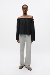 Svart, off-the-shoulder topp med rysjekant og hvite striper, kombinert med lysegrå, utsvingte jeans og svarte sandaler.