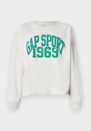 Vaalea harmaa lyhyt takeen pusero pehmeästä kankaasta, jossa on edessä isot, kimaltavat vihreät kirjaimet "GAP SPORT 1969".