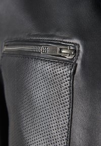 Schwarze Lederjacke aus strukturiertem Material mit einer perforierten Fläche und einer Reißverschlusstasche. Der silberne Reißverschluss passt gut zum Design.
