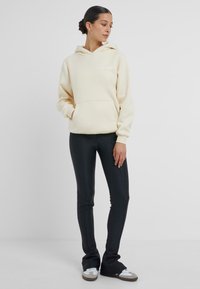 Krämm hoodie med dragsko i huvan, framficka och broderad logo, parat med svarta åtsittande leggings och avslappnade sneakers.