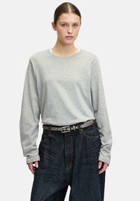 Graues Langarmshirt mit rundem Ausschnitt, kombiniert mit weiten Hosen aus dunklem Denim. Die Hose verfügt über einen genoppten schwarzen Gürtel als zusätzliche Detail.