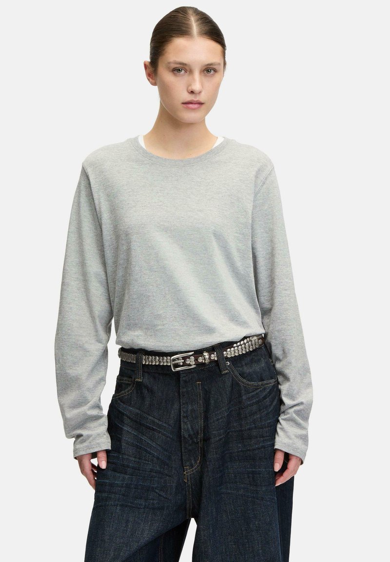 Graues Langarmshirt mit rundem Ausschnitt, kombiniert mit weiten Hosen aus dunklem Denim. Die Hose verfügt über einen genoppten schwarzen Gürtel als zusätzliche Detail.