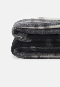 Couverture en polaire grise, pliée. Présente différentes nuances de gris avec une texture douce. Détail des bords visible, créant une finition soignée.