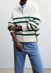 White striped sweater with green horizontal stripes, zippered collar, and ribbed cuffs, paired with light blue denim jeans.