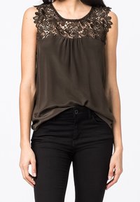 Ärmärmlös mörkbrun topp med blommig spetsdetalj på axlar och övre bröst, bärs med figurnära svarta byxor.