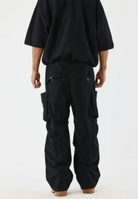 Pantaloni cargo neri con multiple tasche laterali, design a gamba larga e tessuto testurizzato. Presentano bottoni a pressione e una vestibilità rilassata.