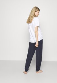 Vit t-shirt med kort ärm som är kombinerad med marinblå byxor i avslappnad passform. Tyget ser mjukt ut; toppen har en enkel rund halsringning och fickor på sidorna.