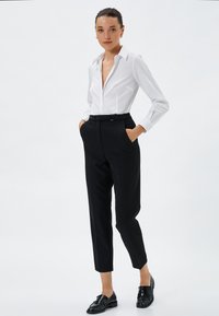 Biała koszula zapinana na guziki z długim rękawem, połączona z czarnymi, dopasowanymi spodniami i czarnymi butami, charakteryzująca się gładką tkaniną i eleganckim wzornictwem.