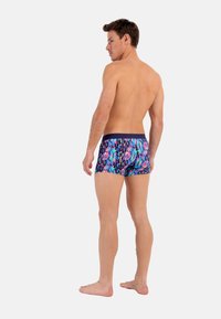 Men's swim shorts in a vibrant multicolored geometric pattern. Features a navy waistband and snug fit, made from lightweight material.