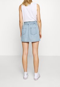 Riflová sukně s elastickým pasem, světle modrá látka, dvě zadní kapsy a rozšířený střih. Nošena s bílými vysokými teniskami.