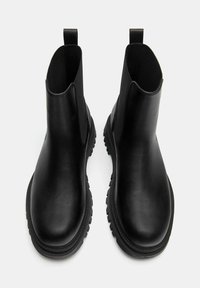 Čierne kožené členkové čižmy s elastickými bočnými panelmi a ťahacími pútkami. Hrubá gumová podrážka s dezénom pre lepšiu priľnavosť. Hladká textúra.