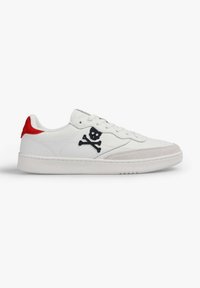 Zapatillas de cuero blancas con acentos rojos en el talón, que presentan un emblema de calavera y tibias cruzadas en negro. Suela de goma texturizada y detalles de costura.