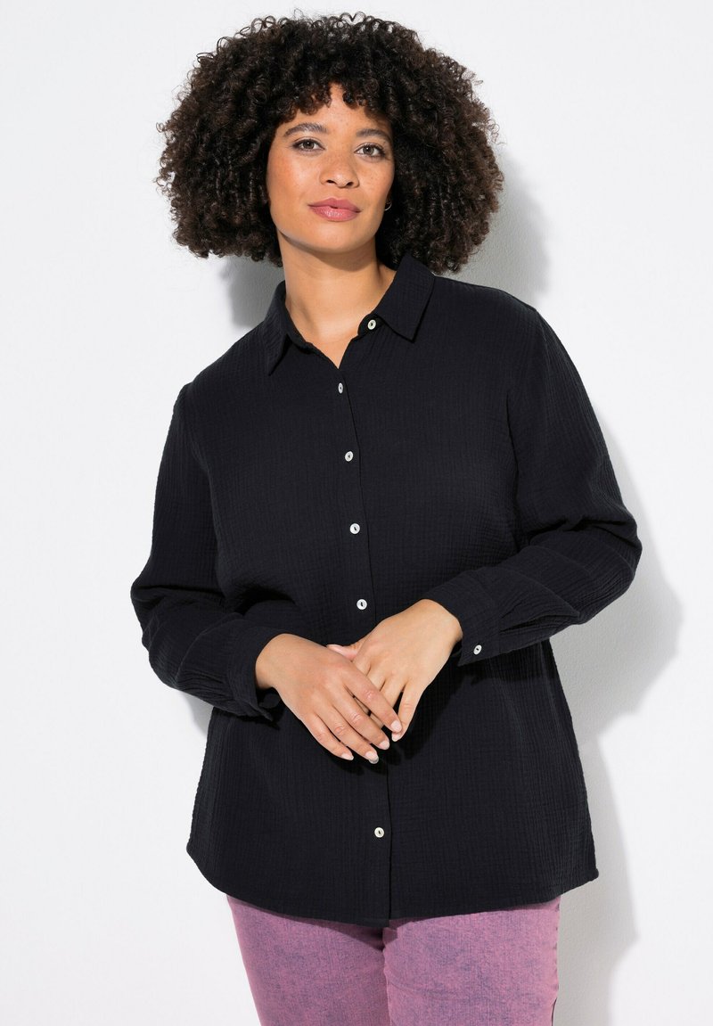 Černá button-up košile vyrobená z texturované tkaniny s límečkem a dlouhými rukávy; obsahuje bílé knoflíky a má volný střih.