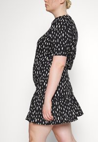 Vestido preto com manchas brancas verticais, mangas curtas e saia ampla. Feito de tecido suave com uma aparência texturizada.