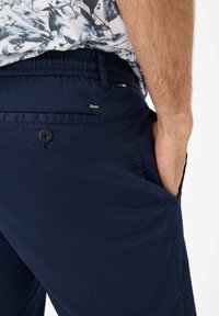Pantaloni da uomo blu navy realizzati in tessuto leggero, con chiusura a bottone, tasche laterali e un discreto logo 'Brax'.