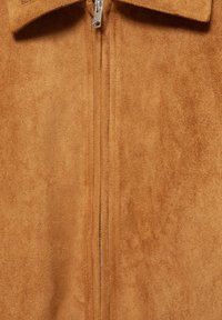 Gros plan d'une veste en daim marron avec une fermeture éclair métallique argentée et un col plié.