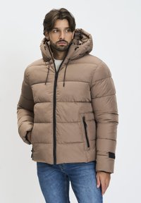 Chaqueta acolchada marrón con capucha, que presenta un diseño acolchado, cremallera frontal y un bolsillo lateral con cremallera negra. Material suave e insulated.