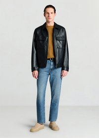 Black leather jacket with two front pockets, worn over a mustard knit sweater, paired with light blue straight-leg jeans and beige slip-on shoes.