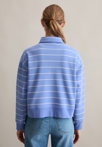 Blauwe gestreepte sweatshirt met een kraag, voorzien van witte horizontale strepen. Het materiaal is zacht met een ontspannen pasvorm, gecombineerd met lichtblauwe jeans.