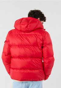 Giacca a piumino rossa con cappuccio, caratterizzata da un design trapuntato e polsini elastici. Tessuto liscio e lucido con vestibilità comoda.